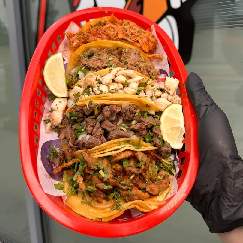 A red basket holds six Space City Birria tacos with various fillings and lime wedges.