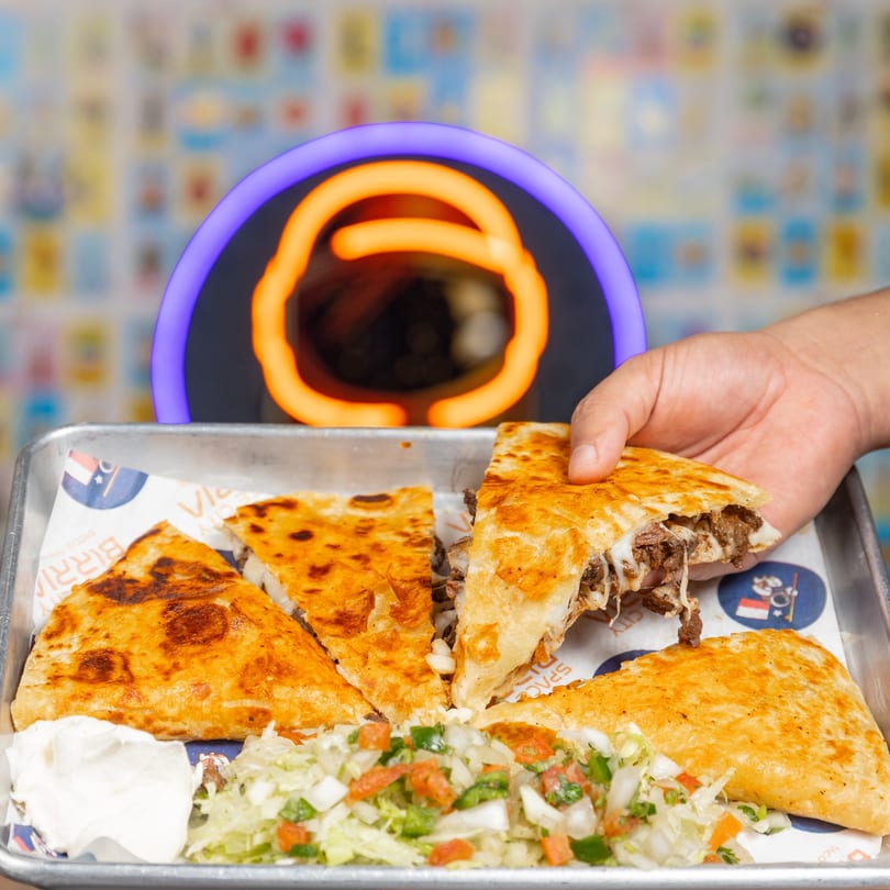 Hand holding a cheesy birria quesadilla slice from Space City Birria, with salsa and sour cream.