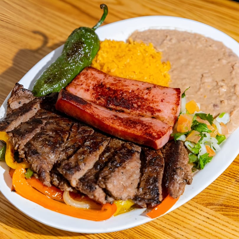 A Space City Birria plate with sliced steak, grilled ham, rice, beans, pico de gallo, and a jalapeño.