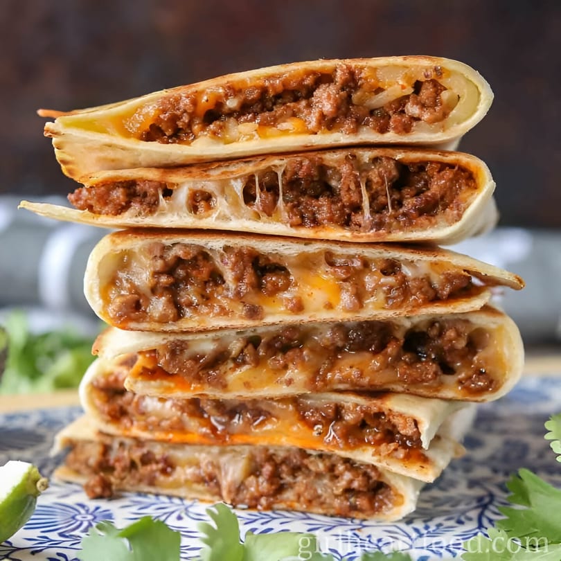 Stack of five Space City Birria quesadillas, filled with meat and melted cheese, on a patterned plate.