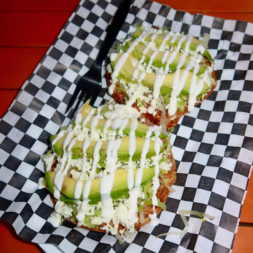 Two Space City Birria tostadas topped with avocado, cheese, and crema on checkered paper.