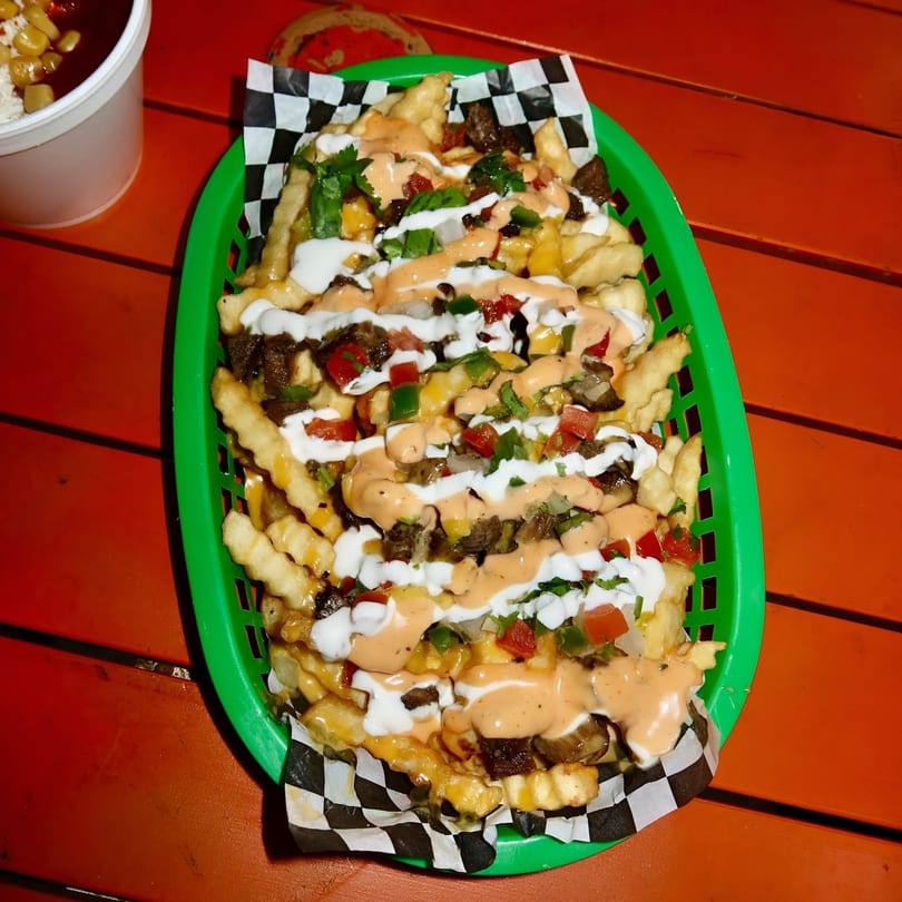 Space City Birria's loaded birria fries with sauces, cheese, and vegetables in a green basket.